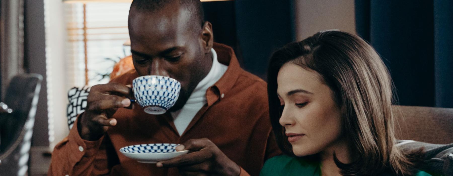 a man and woman sitting on a couch with a cup of tea and a magazine